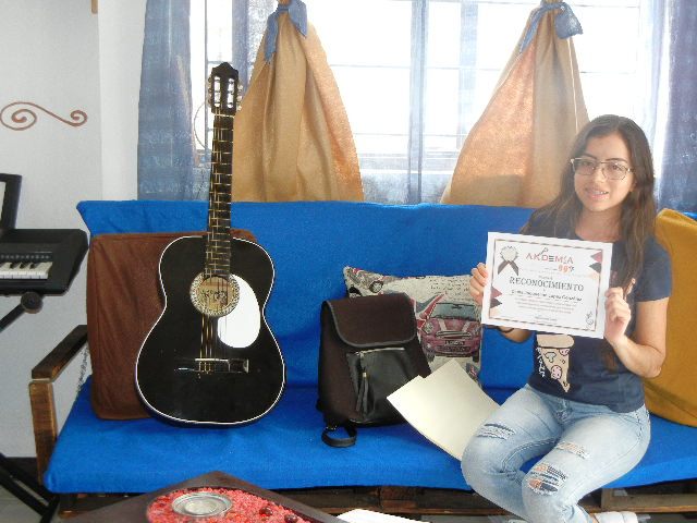 Alumna sosteniendo su reconocimiento junto a su guitarra en Academia 909